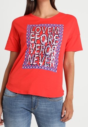 Rood T-shirt met korte mouwen, voorzien van een glinsterende grafische print met de tekst "LOVE ME FOREVER NEVER" tegen een patroonachtergrond.