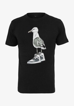 Fekete pamut póló, amelyen egy sneakeres sirály grafikai ábrázolása található. A tervezés vícoloros textúrákat tartalmaz, szürke és fehér árnyalatokkal.