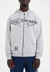 Gray zip-up hoodie featuring a large black "Ed Hardy" logo on the chest, front pockets, and a small black graphic at the hem.