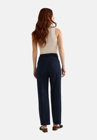 Pantalon à rayures bleu marine avec une coupe droite, associé à un débardeur beige à côtes et des sandales noires à enfiler.