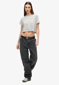 Grijze cropped t-shirt met korte mouwen, gecombineerd met losse zwarte denim broek. Zwarte riem met een zilveren gesp. Casual sneakers met een patroonaccent.