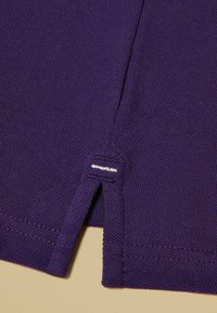 Violeta adīta auduma ar fakturētu rakstu; priekšpusē neliela sānu šķēlums un pie apakšmalas balta dekoratīva šuve.