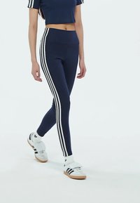 Mornarske tajice s bijelim bočnim prugama, visoki pojas, uparen s bijelim tenisicama s crnim prugama i čičak trakama.