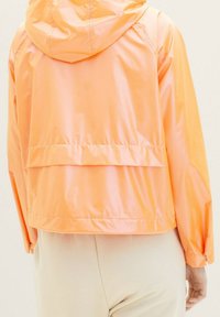 Giacca antipioggia leggera con cappuccio di colore arancione brillante, caratterizzata da una vestibilità comoda, polsini con zip e un design a doppio strato sul retro per una copertura aggiuntiva.