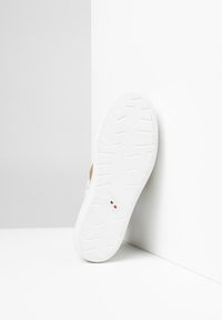 Zapatilla blanca con suela de goma texturizada, con un upper suave y acentos sutiles. Marca italiana notable en la parte inferior.