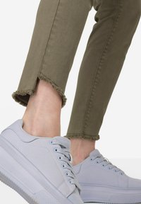 Světle modré plátěné tenisky s plochými tkaničkami a texturovanou podešví, spárované s olivovými džíny s třepenými lemy.