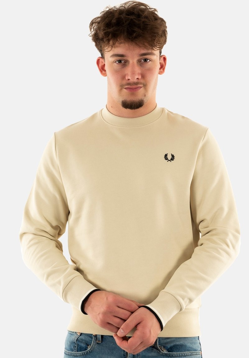 Sudadera beige con mangas largas, cuello redondo, puños acanalados y un pequeño logo negro bordado en el pecho. Textura de tela suave.