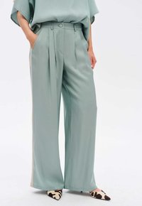 Mintgroene wijde broek gemaakt van een soepele stof, met plooien en een hoge taille. Gecombineerd met puntige schoenen in een koeienprint.