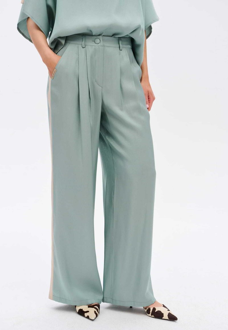 Mintgroene wijde broek gemaakt van een soepele stof, met plooien en een hoge taille. Gecombineerd met puntige schoenen in een koeienprint.