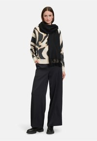 Strikket sweater med et dristigt sort og cremefarvet abstrakt mønster, parret med et sort tørklæde, brede sorte bukser og sorte ankelstøvler.