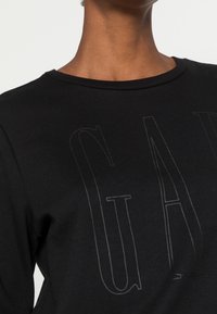 Svart sweatshirt med rund halsringning och subtilt, präglat "GAP"-logotyp i en kontrasterande struktur på framsidan. Mjuk tyg med en slät yta.