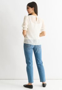 Blusa bianca a pois con maniche a sbuffo, bordo in pizzo sui polsini e un piccolo apertura a chiave sul retro. Abbinata a jeans blu a vita alta e ballerine nere.