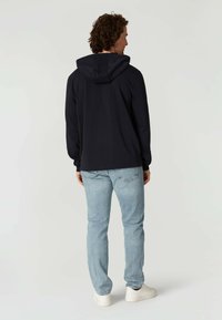 Sudadera con capucha negra de corte relajado, combinada con jeans de mezclilla azul claro y zapatillas blancas. Material suave, diseño minimalista y sin logotipos visibles.