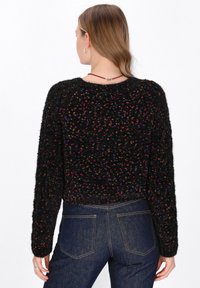 Czarny puszysty sweter z wielokolorowymi drobinkami. Skrócony krój, długie rękawy i okrągły dekolt. Noszony z ciemnoniebieskimi jeansami.