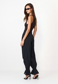 Top negru fără mâneci asociat cu pantaloni largi, cu talie înaltă, de culoare gri închis, ce au manșete volan. Modelul poartă ochelari de soare negri și tocuri.
