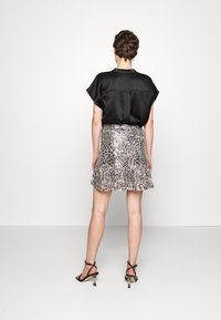 Top in satin nero con maniche a cappuccio corte, abbinato a una gonna argentata con paillettes e orlo a volant, e sandali neri con tacco a strappo.