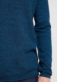Pull bleu tricoté avec un tissu texturé, des manches longues et une coupe décontractée. Le matériau est doux avec un motif subtil.