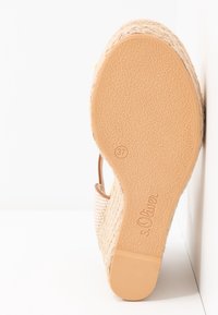 Semelle de sandale compensée montrant une semelle inférieure en caoutchouc texturé taille 37 et marque s.Oliver, dessus tissé beige, positionnée sur fond blanc.