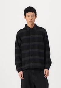 Black and gray plaid shirt jacket, featuring a button front, collar, and long sleeves. Made from soft fabric with a relaxed fit.