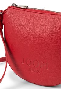 Czerwona skórzana torebka na ramię o fakturze tkaniny, z wytłoczonym logo "JOOP! JEANS" i srebrnymi detalami zamka błyskawicznego.