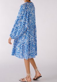 Sininen ja valkoinen kuviollinen mekko, jossa on pitkät hihat, kerroksellinen muotoilu ja rento istuvuus. Materiaali näyttää tekstuuriltaan ja sillä on joustava tiputus.