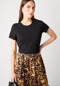 Top corto nero con maniche a sbuffo abbinato a una gonna con stampa leopardata nei toni del beige e del nero, caratterizzata da un elastico in vita e una silhouette fluida.