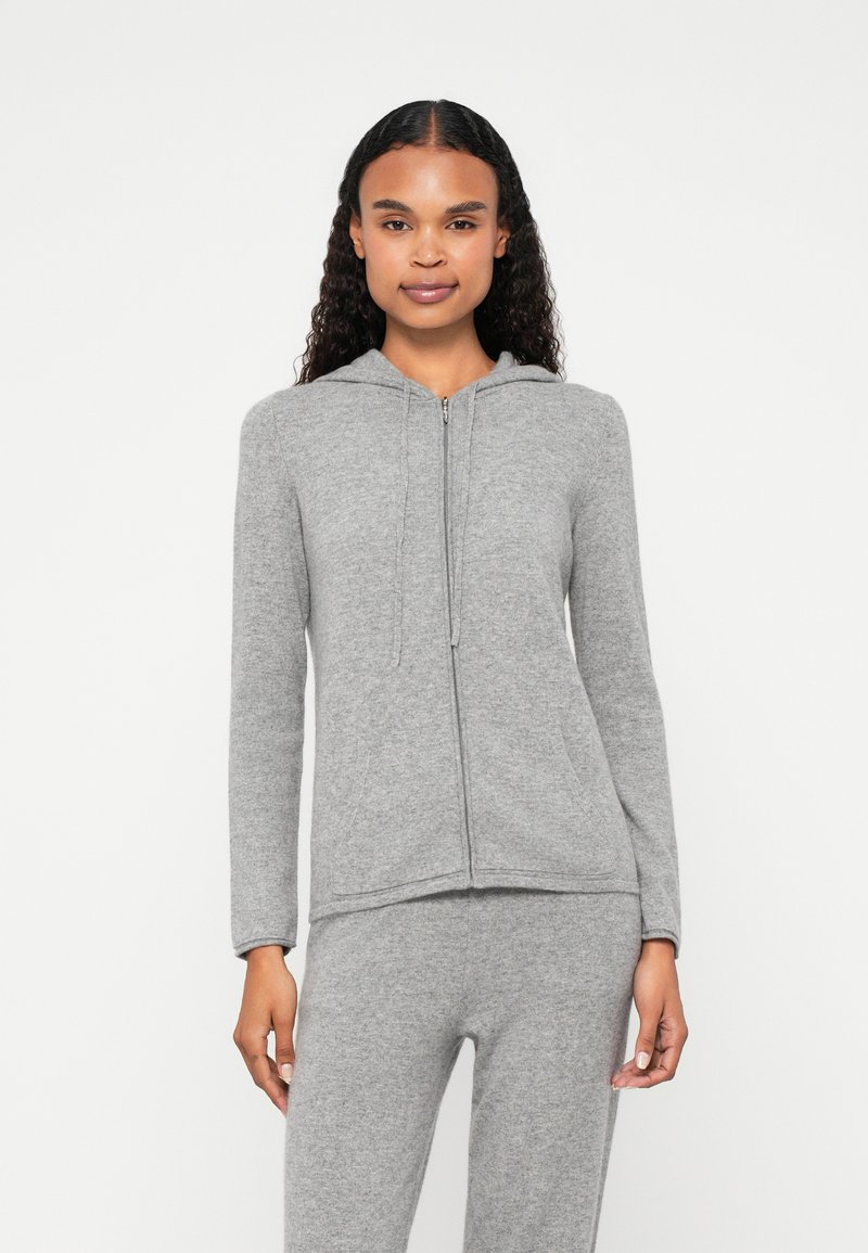 Sweatshirt cinza com fecho, capuz com cordão, mangas longas e uma textura suave; combinado com calças cinzas para um visual coordenado.