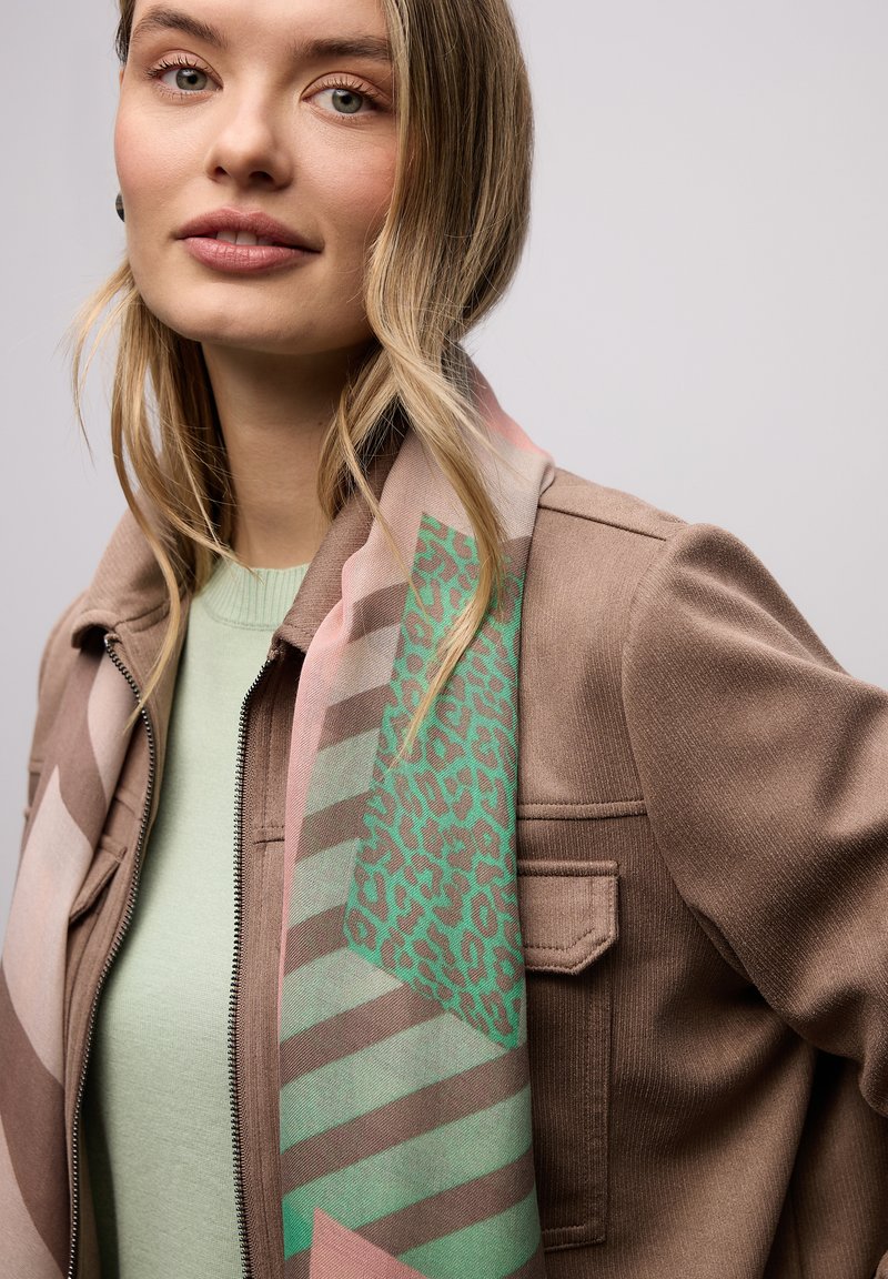 Écharpe multicolore avec imprimé léopard vert et motifs géométriques, drapée sur une veste beige et un haut vert menthe. Texture de tissu lisse.