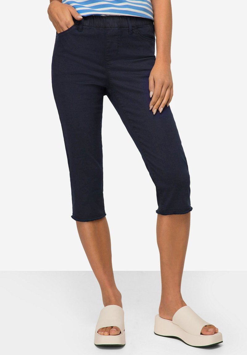 Pantalons courts navy en tissu lisse avec une taille extensible et un détail d'ourlet effiloché, associés à des sandales à plateforme de couleur claire.