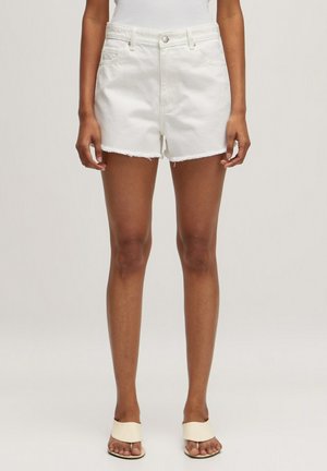 Shorts en denim blancs avec un ourlet effiloché, poches avant et taille ajustée. Associés à des sandales neutres, présentant un design minimaliste.
