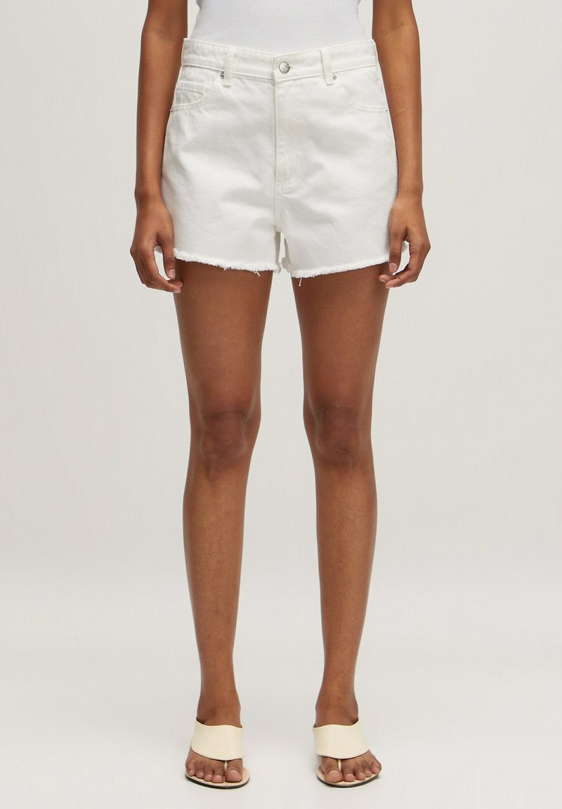 Witte denimshorts met een rafelige zoom, voorzakken en een getailleerde taille. Gecombineerd met neutrale sandalen, die een minimalistisch ontwerp tonen.