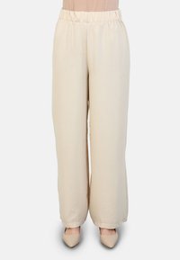 Beige wide-leg pants made from textured fabric with an elastic waistband and an ankle-length cut, paired with pointed toe heels.