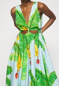 Blomsterkjole i lys blå med grønne bananblad- og gule frugtmønstre. Har en dyb udskæring og et skåret talje-design.