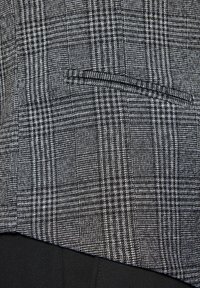 Czarnobiała tkanina w kratkę o teksturowanej powierzchni i kieszeni na brzegu. Wzór składa się z małych kwadratów i linii.