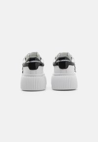 Weiße Sneakers mit dicker, gerippter Sohle, schwarzen Akzenten an der Ferse und geprägtem Logo. Obermaterial aus glattem Leder mit minimalistischem Design.
