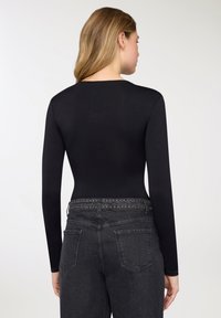 Body nero a maniche lunghe con texture liscia, caratterizzato da collo arrotondato e design aderente, abbinato a jeans in denim scuro con vita borchiata.