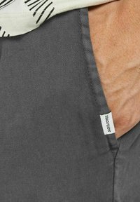 Harmaat puuvillaiset housut, joissa on sivutasku, jossa on "JACK & JONES" -labeli. Tekstuuri näyttää pehmeältä ja hieman karhealta.