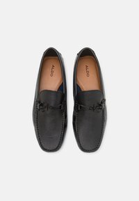 Mocassins en cuir noir avec une finition texturée, doublure en cuir marron et quincaillerie décorative avec lacets. Design classique, style slip-on.
