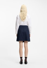 Witte blouse met lange mouwen, achteraanzicht, gecombineerd met een marineblauwe rok met krijtstrepen. Glad textuur, op maat gemaakte pasvorm, en geaccentueerde taille.