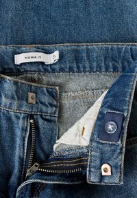 Denimist sinised teksapüksid, millel on tõmblukuga lend, metallist nööp sulgemiseks ja sisemine valge vooder sildilabelliga.