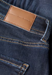 Ciemnoniebieskie dżinsy z denimu z skórzaną metką oznaczoną "STREET ONE STUDIO", wyróżniające się wyraźnym widocznością szwów i gładką fakturą.