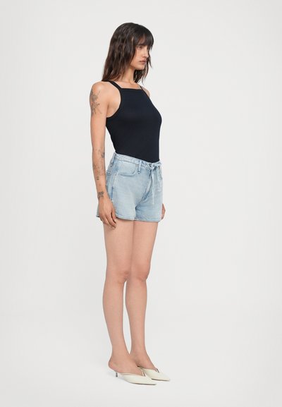 Bodysuit noir sans manches associé à un short en jean bleu clair. La tenue est complétée par des chaussures blanches et présente des coutures délicates.