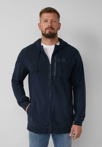 Felpa con zip di colore blu navy, dotata di tasca frontale, cappuccio con cordino e tessuto morbido. Presenta polsini e orlo a costine, con dettagli di cuciture piatte.