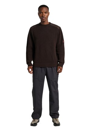 Dunkelbrauner, gerippter Strickpullover mit Rundhalsausschnitt und strukturiertem Stoff, kombiniert mit locker sitzenden schwarzen Hosen und grauen Wanderschuhen.