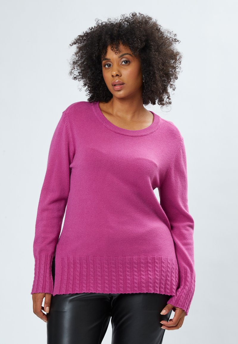 Lyserød strikket sweater med rund hals og ribbede kanter. Har lange ærmer og sideslidser, lavet af et blødt, struktureret stof.