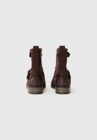 Bottines en cuir marron avec une texture lisse, des fermetures éclair sur le côté et un petit talon en bois empilé. Se distingue par une sangle décorative sur le côté.