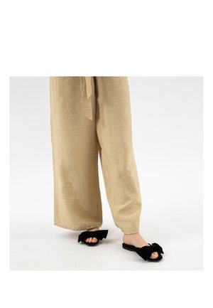 Pantaloni beige a gamba larga abbinati a sandali neri con punta aperta e grandi fiocchi di tessuto sopra.