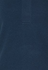 Tissu de pull en maille bleu marine avec une texture côtelée et un patch rectangulaire central. Matière douce et extensible.