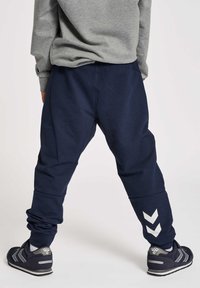 Dunkelblaue Jogginghosen mit einer lockeren Passform, versehen mit weißen Chevron-Akzenten an den Unterschenkeln. Hergestellt aus einem weichen, glatten Stoff.