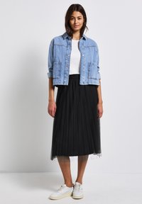 Ljust blå denimjacka med fickor, vit t-shirt, svart veckad tyllkjol och vita sneakers. Enkelt och lager-på-lager design.